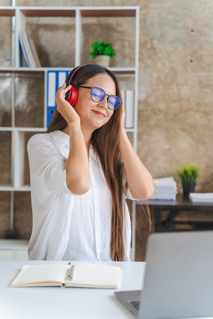 Jovem mulher asiática usando fones de ouvido trabalhadora freelancer e computador portátil ele ouvindo rádio de música