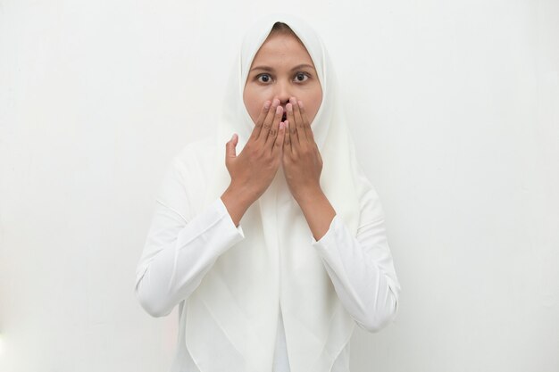 Jovem mulher asiática usando hijab chocada cobrindo a boca com as mãos por engano