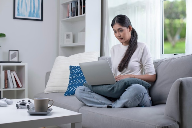 Jovem mulher asiática usando laptop em casa olhando para a tela conversando lendo ou escrevendo e-mail sentada na mesa aluna séria fazendo lição de casa trabalhando em projeto de pesquisa on-line