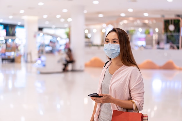 Jovem mulher asiática usando máscara cirúrgica fazendo compras em loja de roupas em shopping