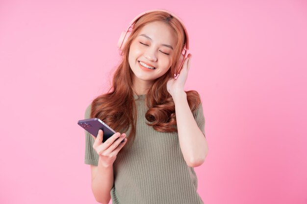 Jovem mulher asiática usando smartphone e ouvindo música em fundo rosa
