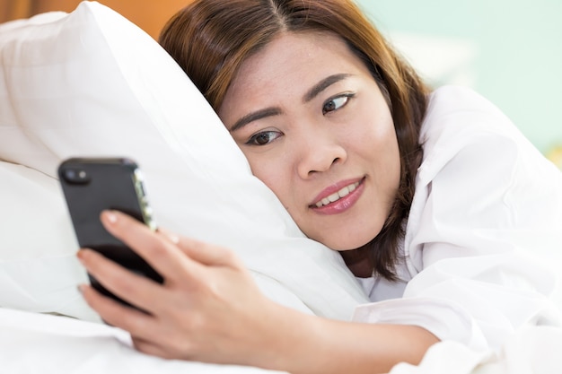 Jovem mulher asiática usando smartphone na cama branca.