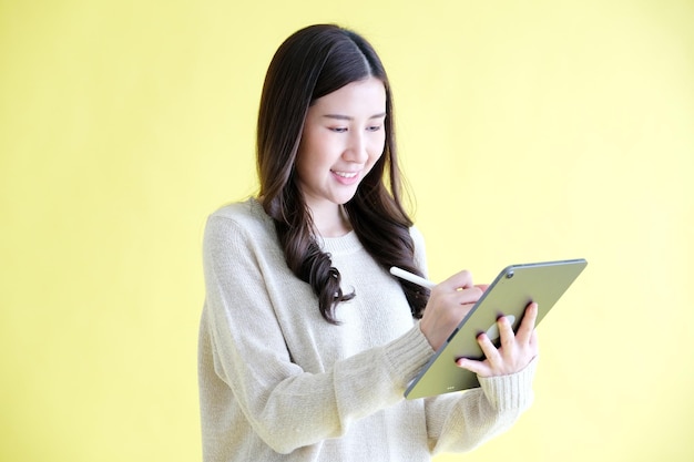 Jovem mulher asiática usando tablet digital em pé sobre fundo amarelo isolado