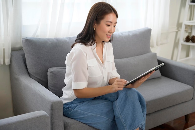 Jovem mulher asiática usando tablet no sofá na sala x9