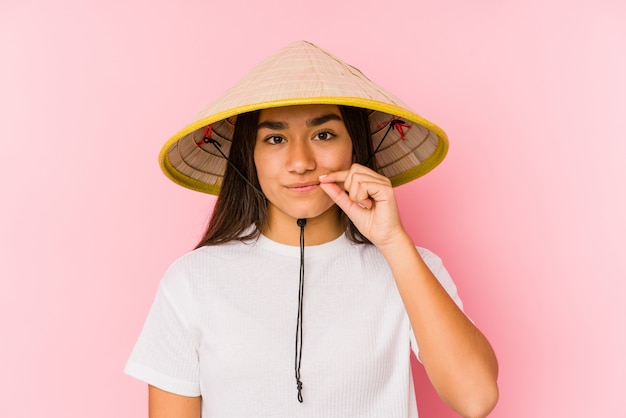 Foto jovem mulher asiática usando um chapéu vietnamita com os dedos nos lábios, mantendo um segredo.