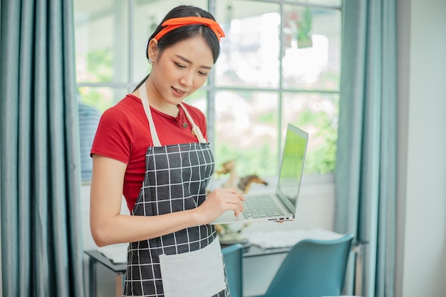 Jovem mulher asiática usando um computador para cozinhar na cozinha