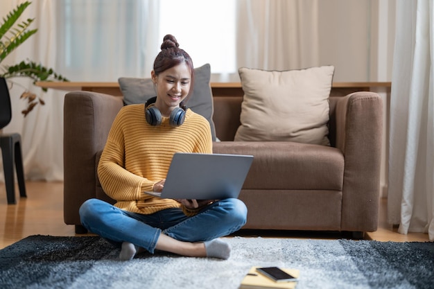 Jovem mulher asiática vestida casualmente trabalhando no laptop enquanto está sentado no chão em casa Trabalhe em casa no conceito de atmosfera aconchegante