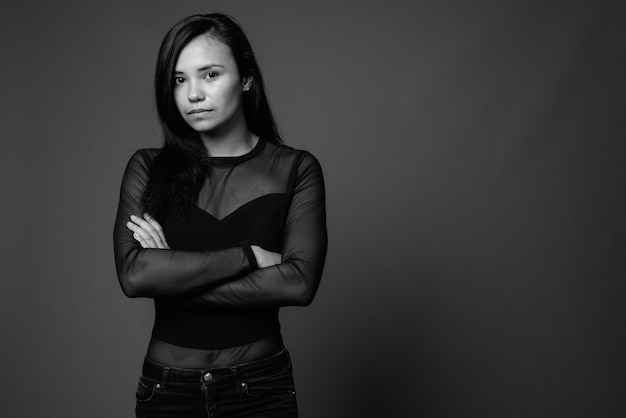 jovem mulher asiática vestindo camisa preta de mangas compridas contra a parede cinza. Preto e branco
