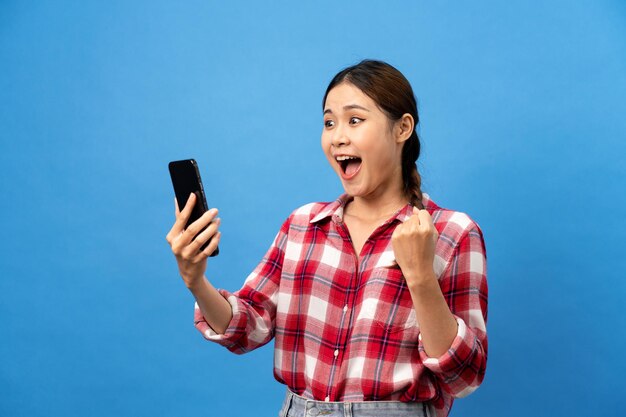 Foto jovem mulher asiática vestindo camisa vermelha de guingão com penteado de trança e olhando no smartphone com sentimento