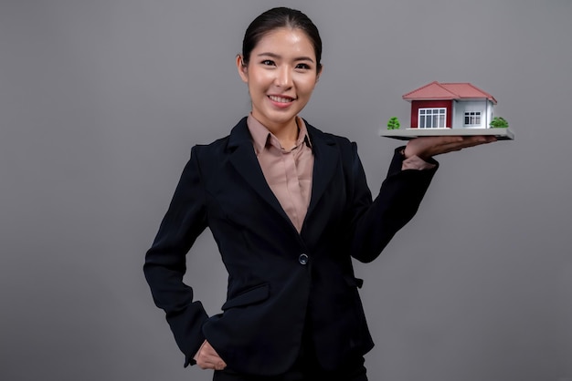 Jovem mulher asiática vestindo terno formal segurando modelo de casa Entusiasmado