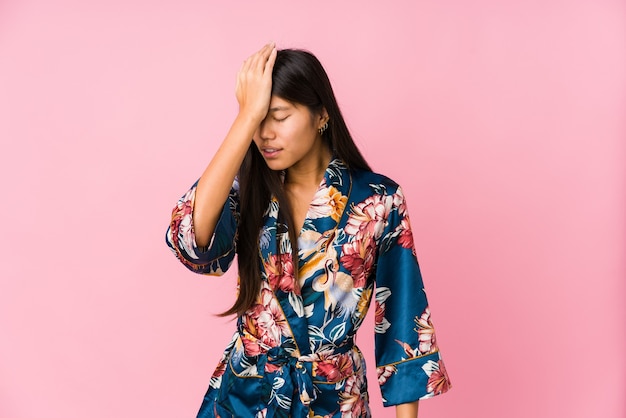 Jovem mulher asiática vestindo um pijama de quimono, esquecendo de algo, batendo na testa com a palma da mão e fechando os olhos.