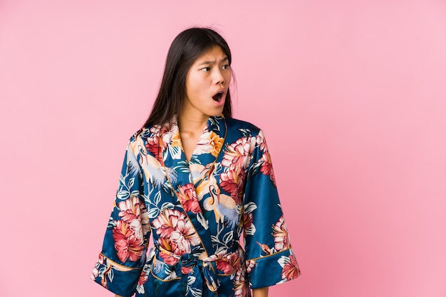 Jovem mulher asiática vestindo um pijama de quimono sendo chocada por causa de algo que ela viu.