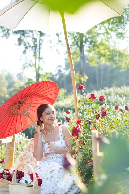 Jovem mulher asiática vestindo um vestido branco posa com uma rosa no jardim de rosas