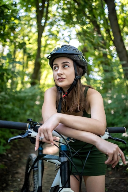 Jovem mulher ativa sexy de vestido verde fica perto de bicicleta na floresta Estilo de vida de atividade no dia de verão