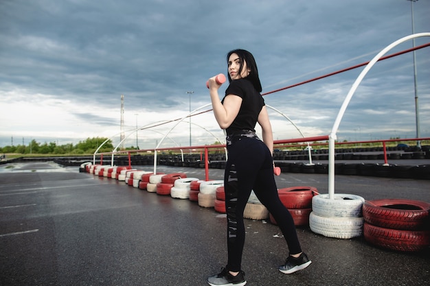 Jovem mulher atlética com cabelos longos, fazendo exercícios com halteres no playground ao ar livre. Cuidados de saúde, conceito de esportes. Esportes durante a quarentena