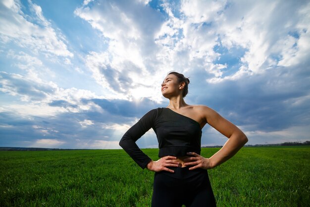 Jovem mulher atlética construir com uma blusa preta e leggings pretas sobre um fundo de céu azul. estilo de vida saudável, menina morena atlética. o conceito e a motivação dos esportes