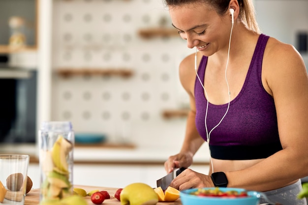 Foto jovem mulher atlética feliz cortando frutas e fazendo uma refeição saudável na cozinha