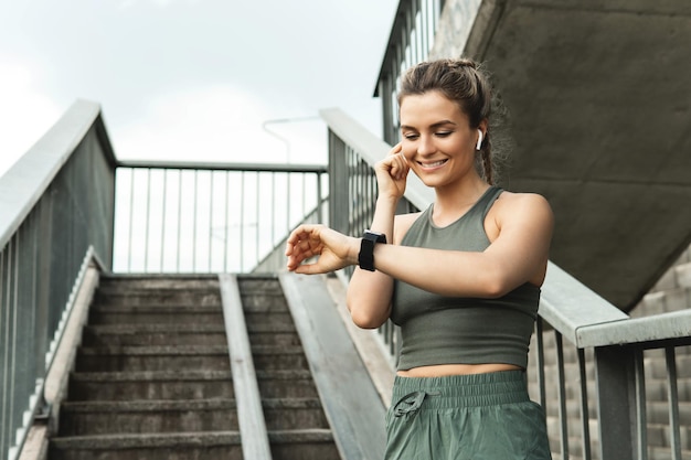 Jovem mulher atlética usando smartwatch durante seu treino de fitness na rua da cidade