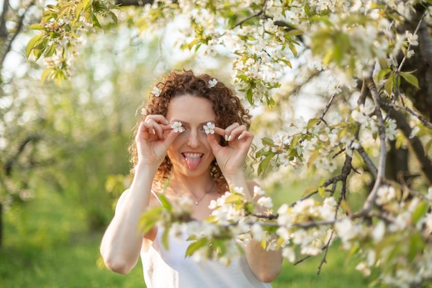 Jovem mulher atraente caminha no parque verde primavera, apreciando a natureza de floração. Mulher sorridente saudável girando no gramado da primavera.