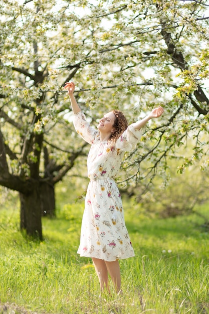 Jovem mulher atraente caminha no parque verde primavera, apreciando a natureza de floração