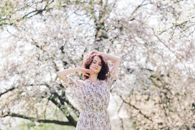 Jovem mulher atraente com cabelo comprido encaracolado, posando no jardim florido de primavera, macieiras