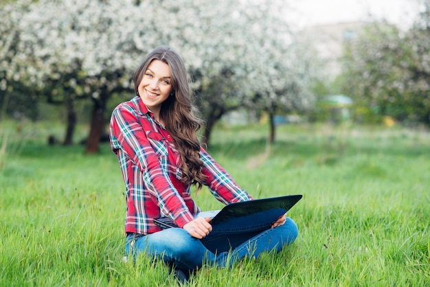 Jovem mulher atraente com laptop na grama no jardim florescendo