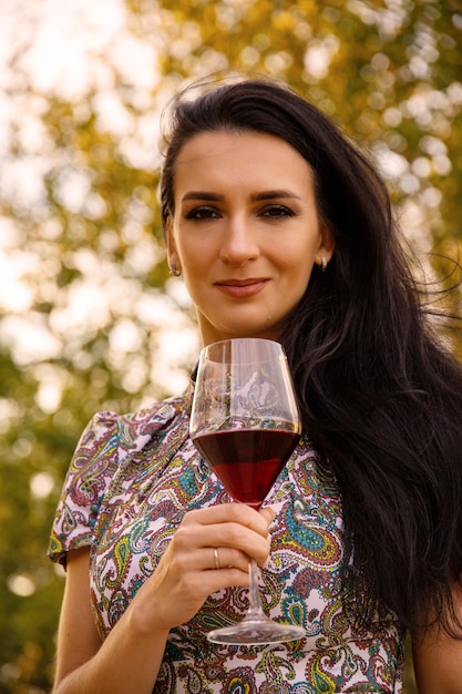 Jovem mulher atraente com uma taça de vinho tinto na natureza