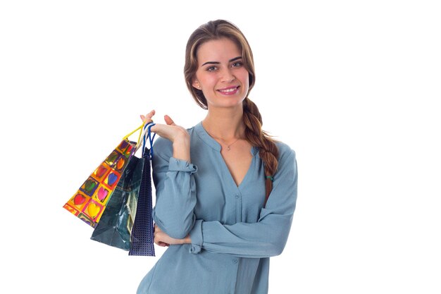 Jovem mulher atraente de blusa azul segurando sacolas de compras multicoloridas em fundo branco no estúdio