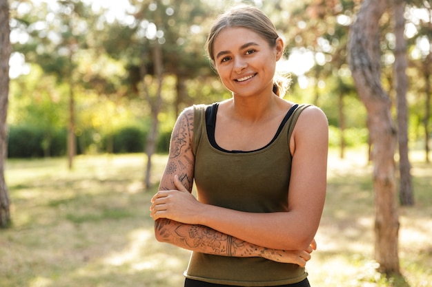 jovem mulher atraente em roupas esportivas olhando e sorrindo enquanto se exercita no ensolarado parque verde