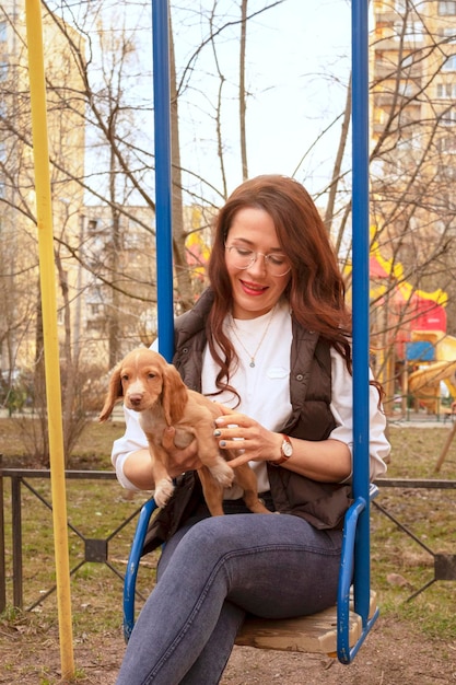 Jovem mulher atraente em um balanço com um filhote de cocker spaniel bonito. Um novo membro fofo da família. Cuidados com animais de estimação e conceito de animais de estimação