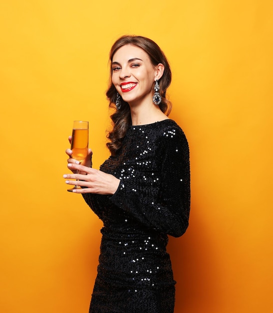 Foto jovem mulher atraente em vestido de noite segurando a taça de champanhe sobre fundo amarelo