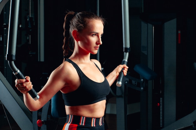 Jovem mulher atraente fazendo exercícios para os braços em uma máquina de treinamento