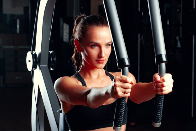 Jovem mulher atraente fazendo exercícios para os braços em uma máquina de treinamento