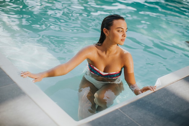 Jovem mulher atraente goza na piscina ao ar livre no horário de verão