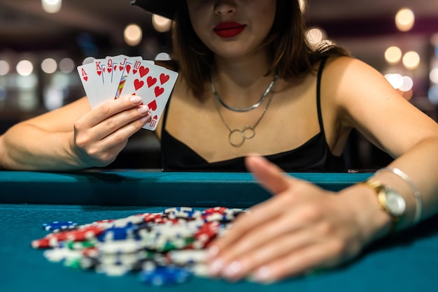 Jovem mulher atraente jogando pôquer na mesa com pilhas de fichas e cartas