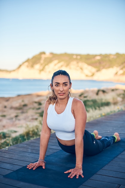 Jovem mulher atraente pratica ioga na pose de cobra na praia.