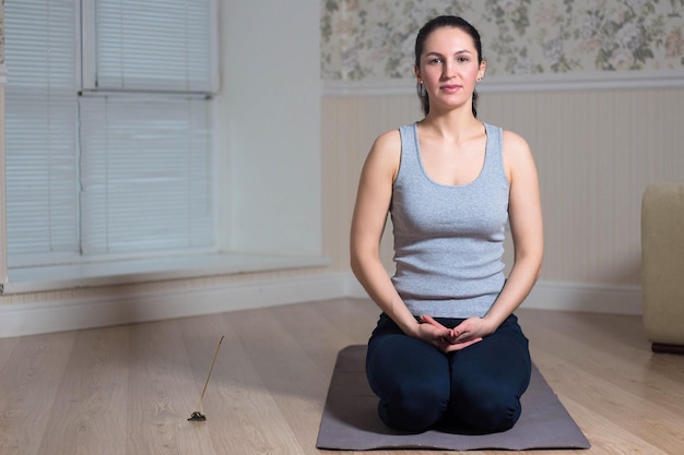 Jovem mulher atraente praticando ioga sentada usando sessão de meditação esportiva interior em casa