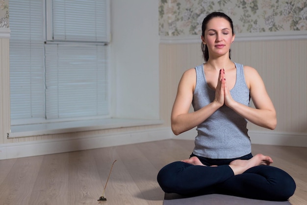 Jovem mulher atraente praticando ioga sentada usando sessão de meditação esportiva interior em casa