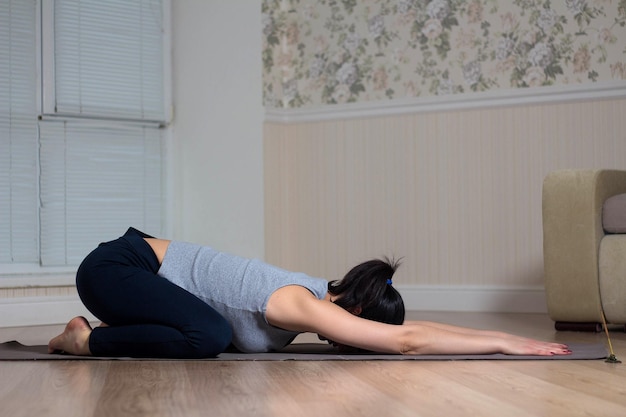 Jovem mulher atraente praticando ioga usando sessão de meditação esportiva interior em casa
