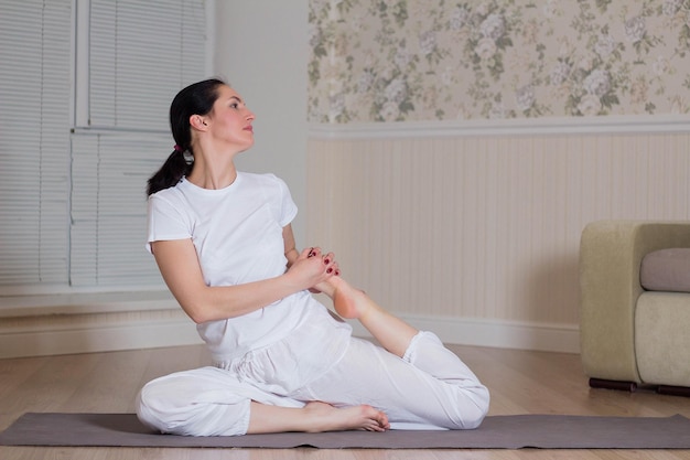 Jovem mulher atraente praticando ioga usando sessão de meditação esportiva interior em casa