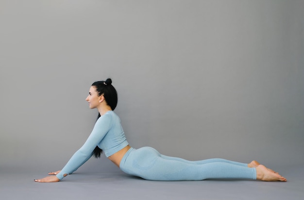 Jovem mulher atraente praticando o conceito de yoga alongamento em cobra exercício bhujangasana pose workout blue sportswear camiseta de manga comprida e calças