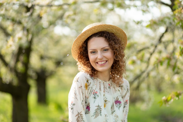 Jovem mulher atraente retrato com cabelos cacheados no chapéu de vime elegante gosta de florescer jardim verde em dia de primavera