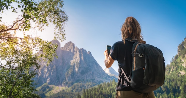 Jovem mulher atraente tirando uma foto com seu celular caminhando em uma bela montanha no verão