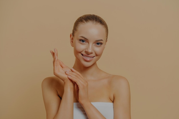 Jovem mulher atraente usando creme para as mãos para manter a pele hidratada tocando as mãos após o banho de cera de parafina