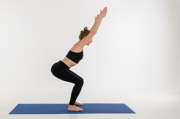 Jovem mulher atrativa desportiva que faz a prática da ioga no fundo branco. Kursiasana.