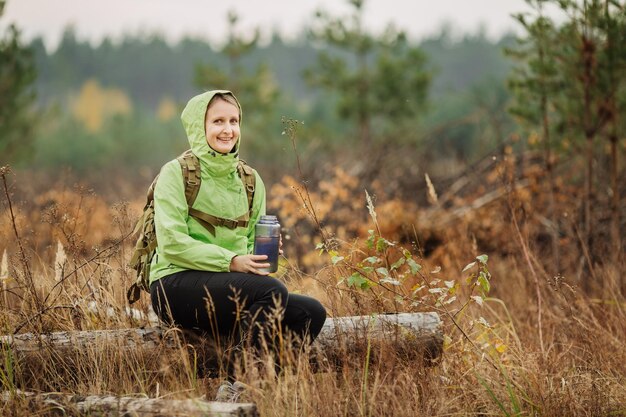 Jovem mulher bebendo água com mochila no vale da floresta