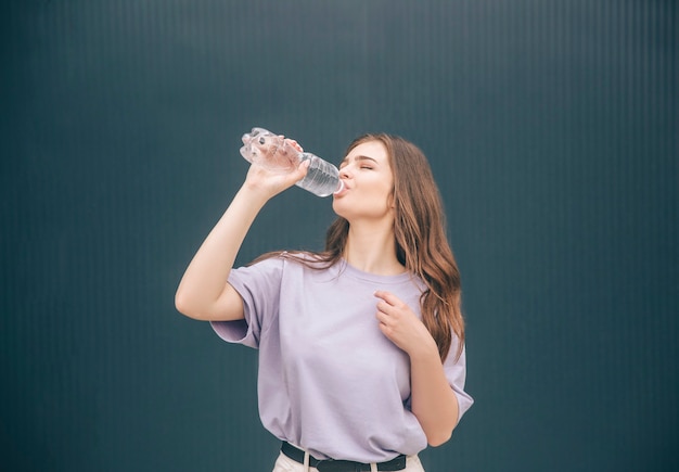 Jovem mulher bebendo água limpa e saborosa em uma garrafa de plástico transparente