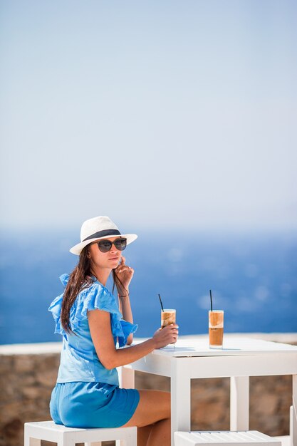 Jovem mulher bebendo café frio, apreciando a vista para o mar.