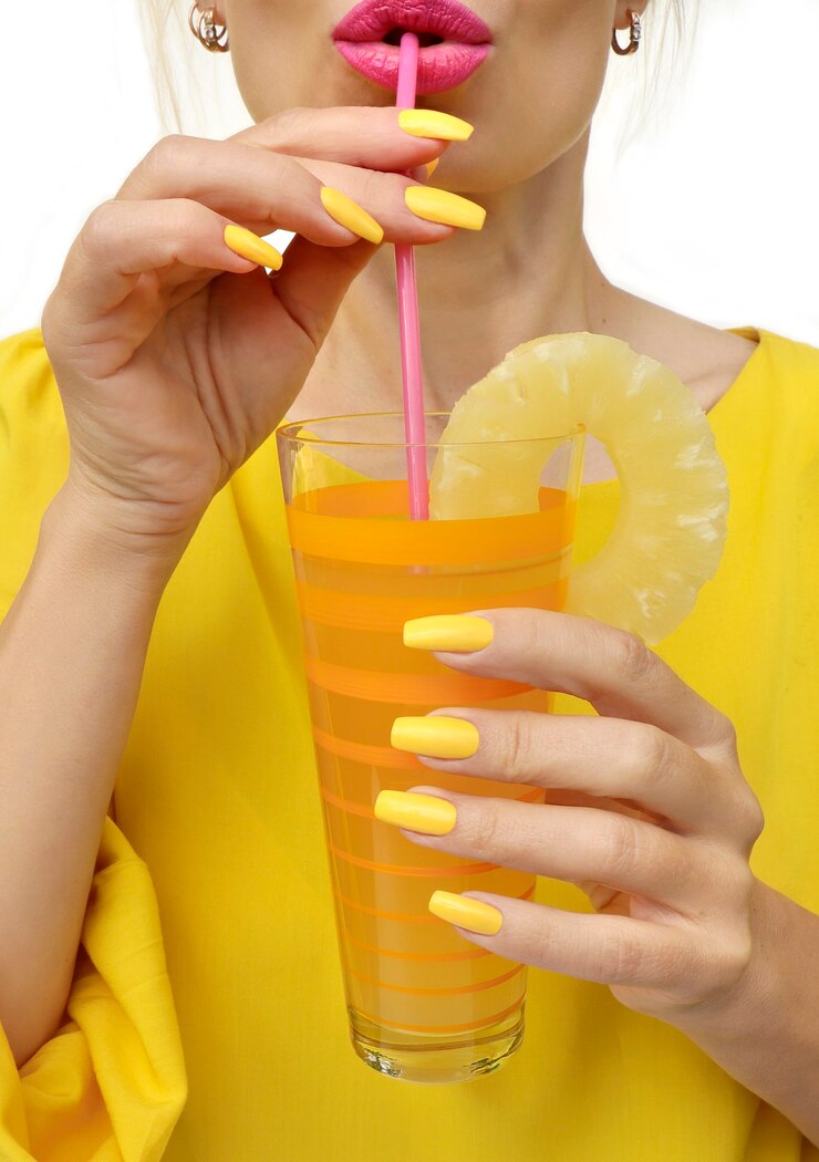 Foto jovem mulher bebendo suco de abacaxi com alegria. manicure moderna com esmalte amarelo em um formulário longo.