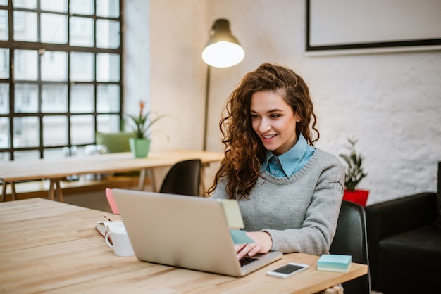 Jovem mulher bem sucedida no escritório moderno que trabalha no portátil.